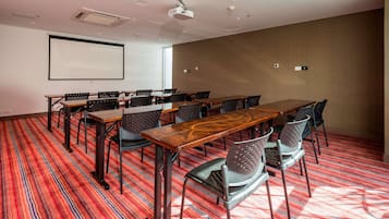 A conference room with a large screen, multiple tables, and chairs.