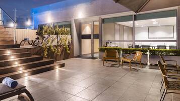 Un patio exterior moderno con una escalera que lleva a un nivel superior, una zona de estar con sillas y una barra.