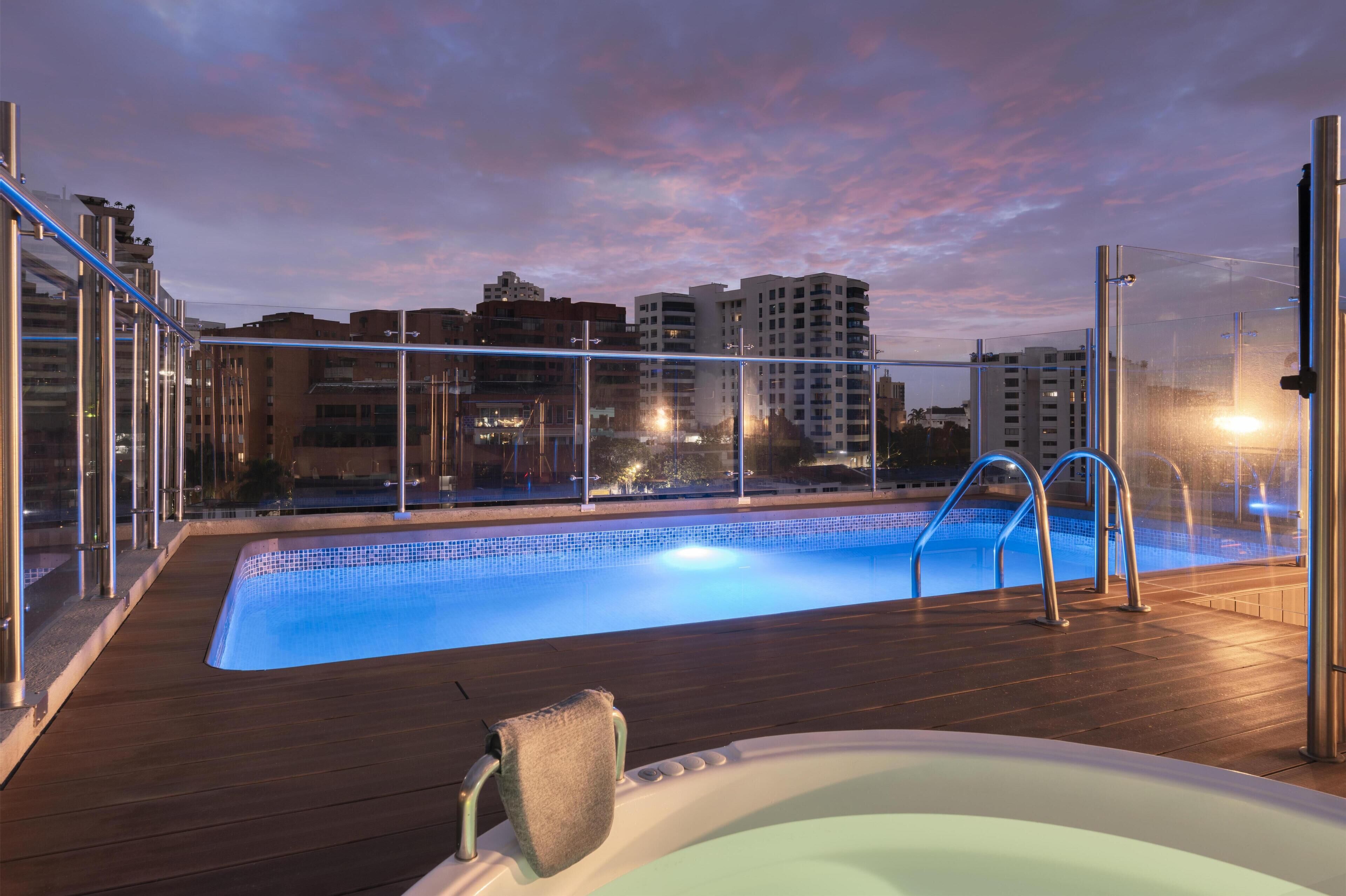 Una piscina en la azotea con vistas a edificios de la ciudad al atardecer.