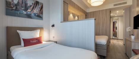 A hotel room with a bed, a desk, a chair, a painting on the wall, and a hallway leading to another room.
