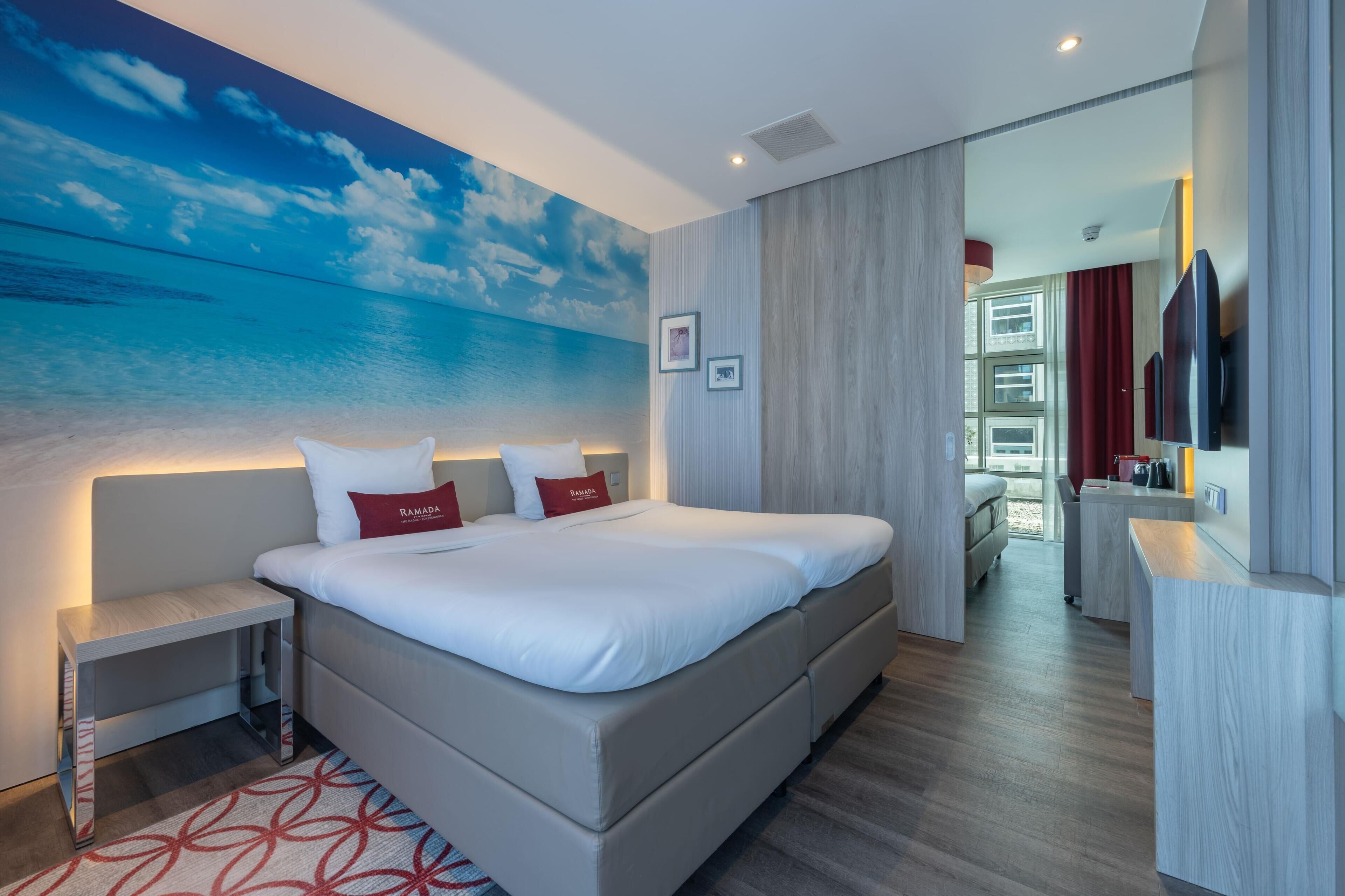 Ein modernes Hotelzimmer mit einem großen Bett, Nachttischen, einem Flachbildfernseher und Meerblick durch ein großes Fenster.