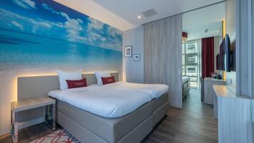 Ein modernes Hotelzimmer mit einem großen Bett, Nachttischen, einem Flachbildfernseher und Meerblick durch ein großes Fenster.
