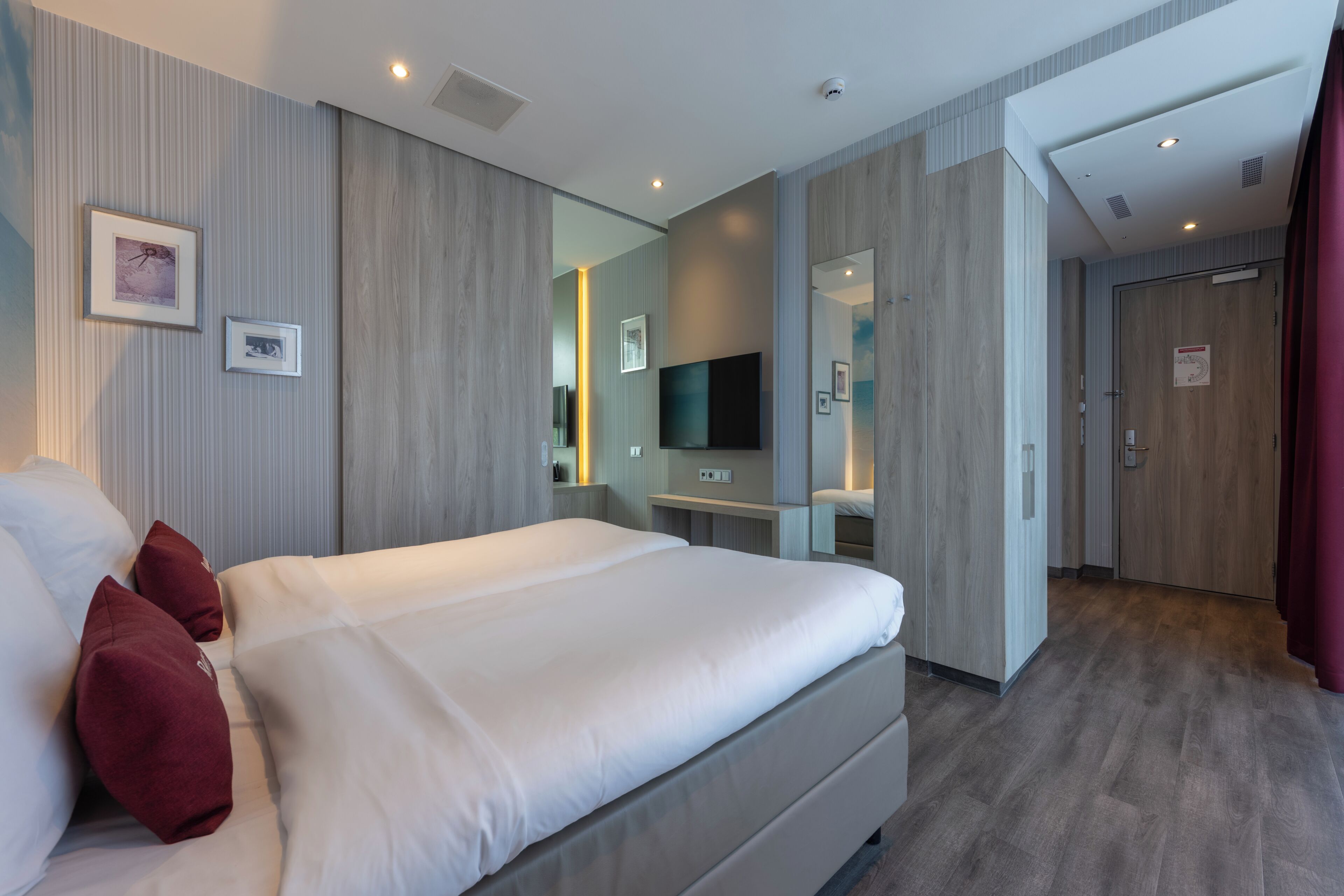 A modern hotel room with a large bed, a flat-screen TV, a bedside table, and a mirror.