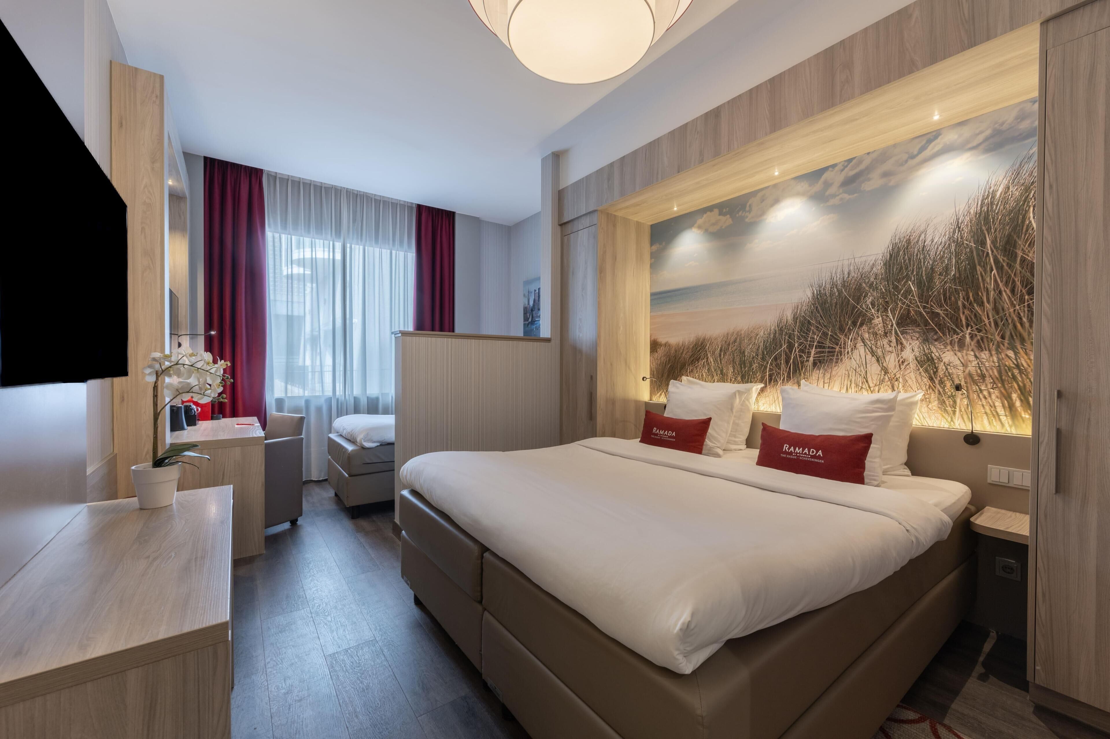 Une chambre d’hôtel avec un grand lit, un bureau, une chaise, une télévision et une fenêtre avec des rideaux.