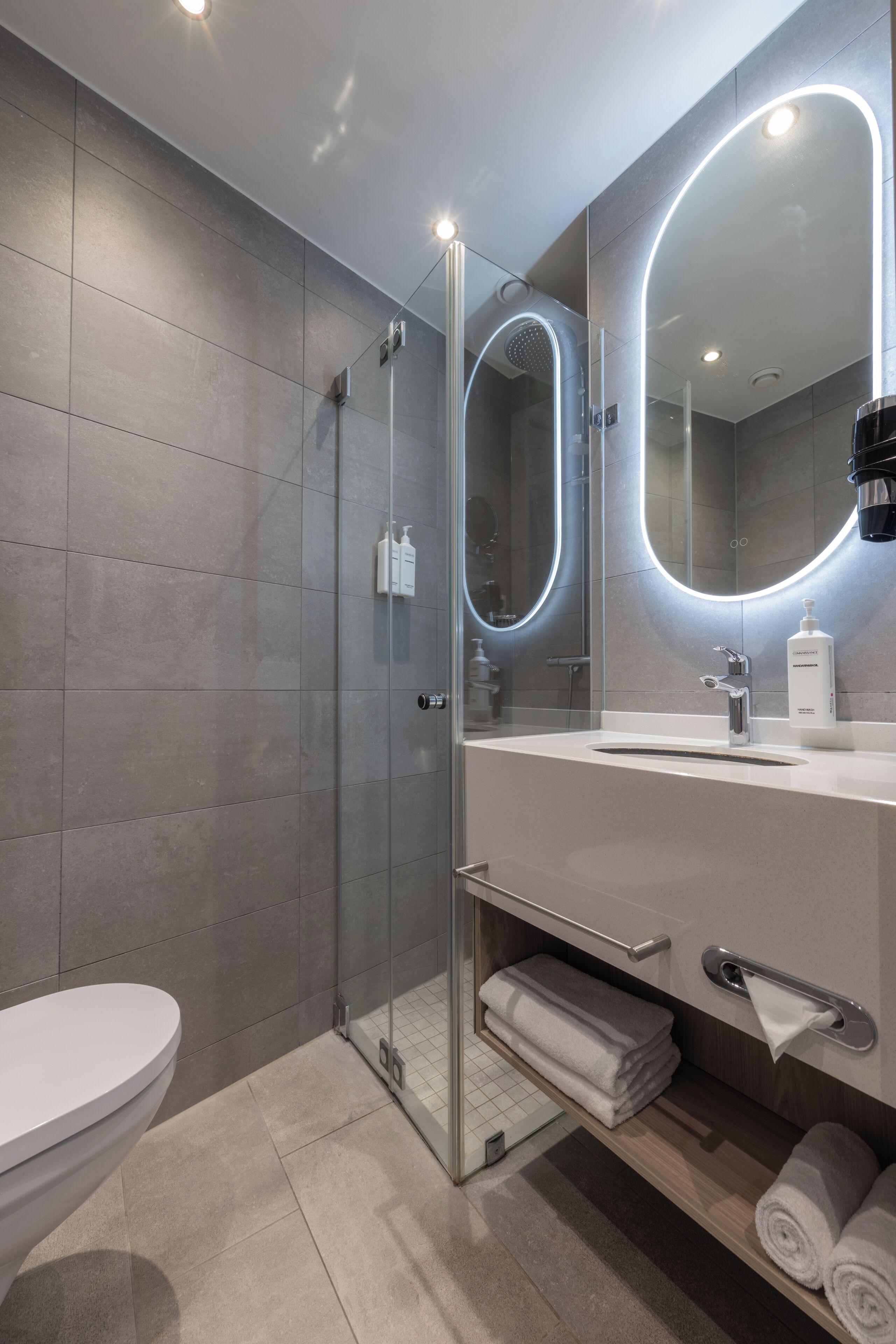 A modern bathroom with a glass-enclosed shower, a white sink, and a large mirror with built-in lighting.