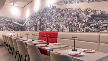 A restaurant with a cityscape mural, booths, and tables with plates and cutlery.