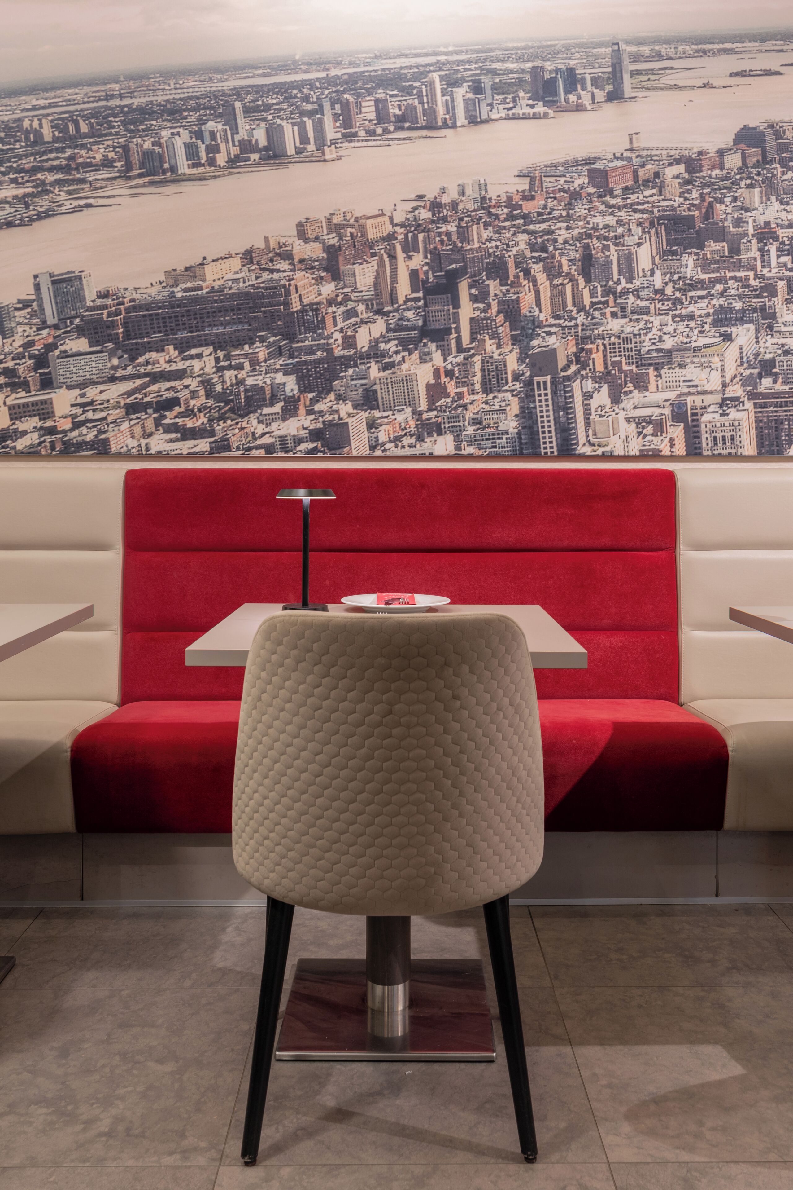 Un comedor con un banco rojo, una mesa y una silla, con vista a un paisaje urbano.