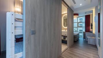 Een moderne hotelkamer met een houten vloer, een inbouwkleerkast, een badkamer met spiegel en een zithoek met televisie.