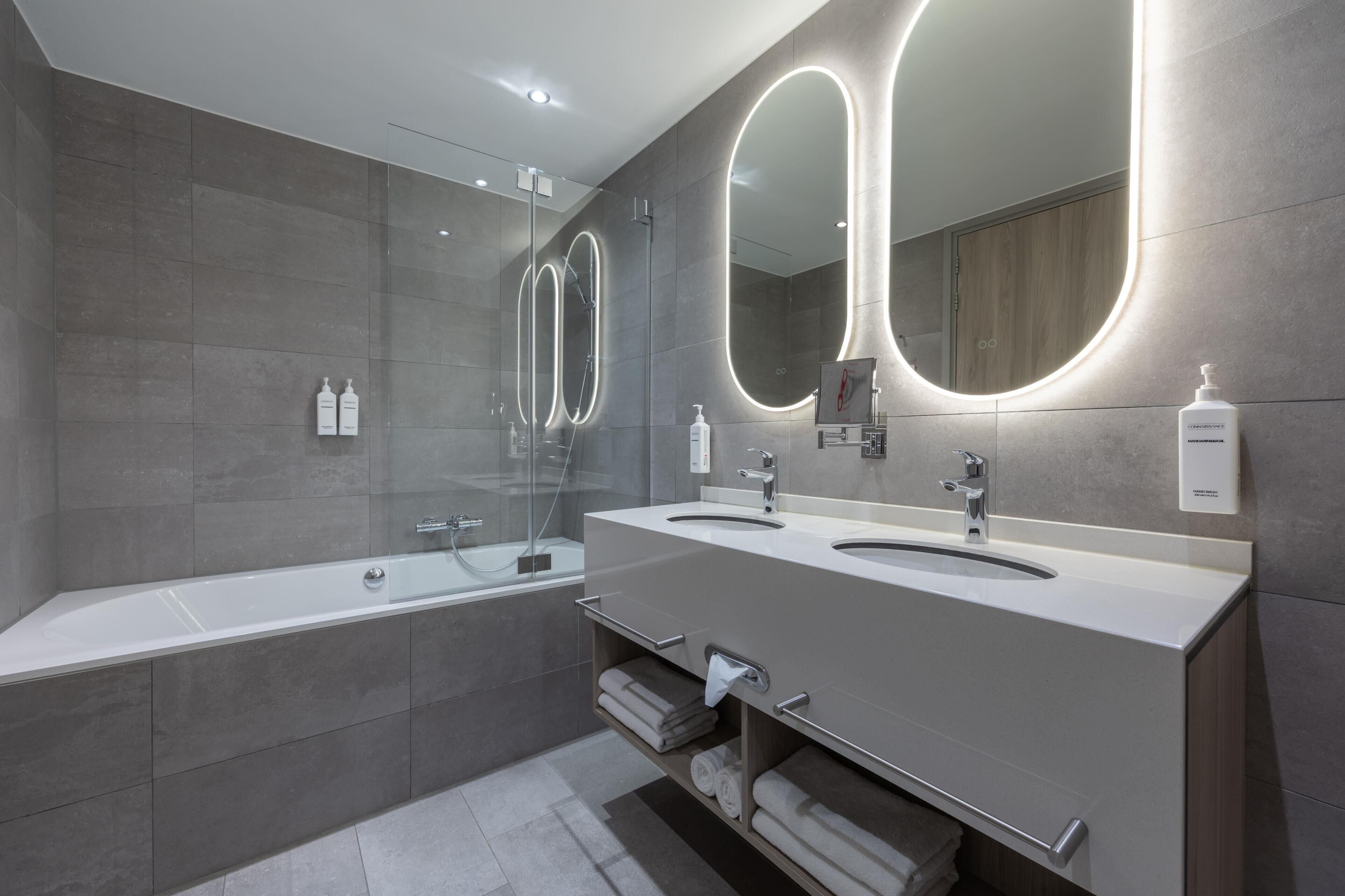 A modern bathroom with two sinks, a large mirror, and a glass-enclosed shower.