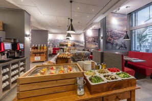 Een ontbijtruimte van een hotel met diverse eetmogelijkheden, zoals fruit, gebak en drankjes.