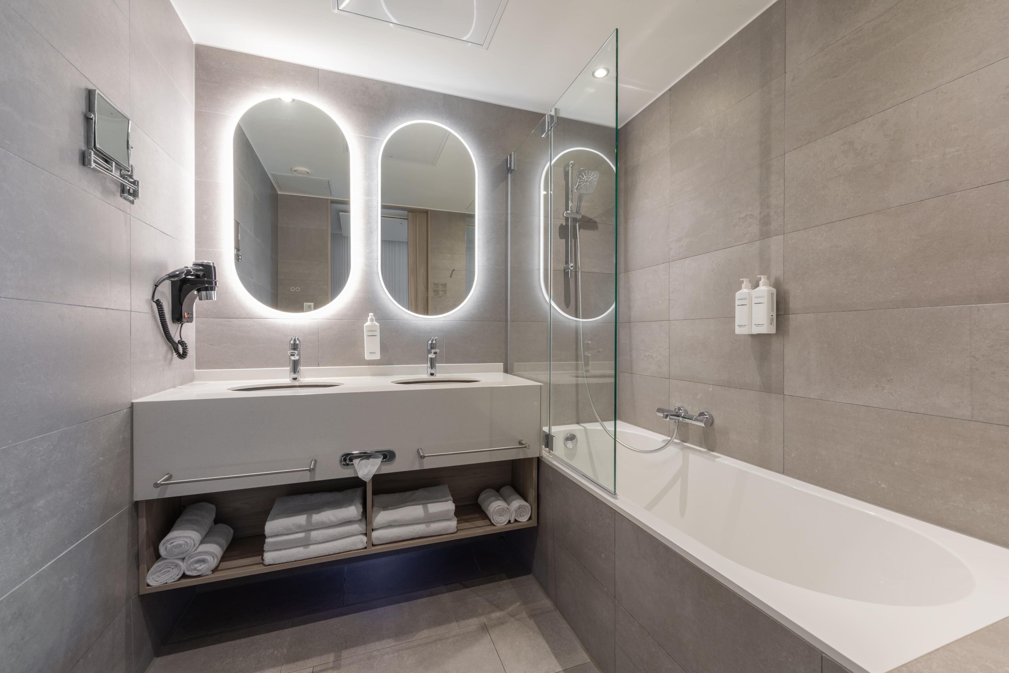 Ein modernes Badezimmer mit großem Spiegel, zwei Waschbecken, einer Badewanne und einem Handtuchhalter.