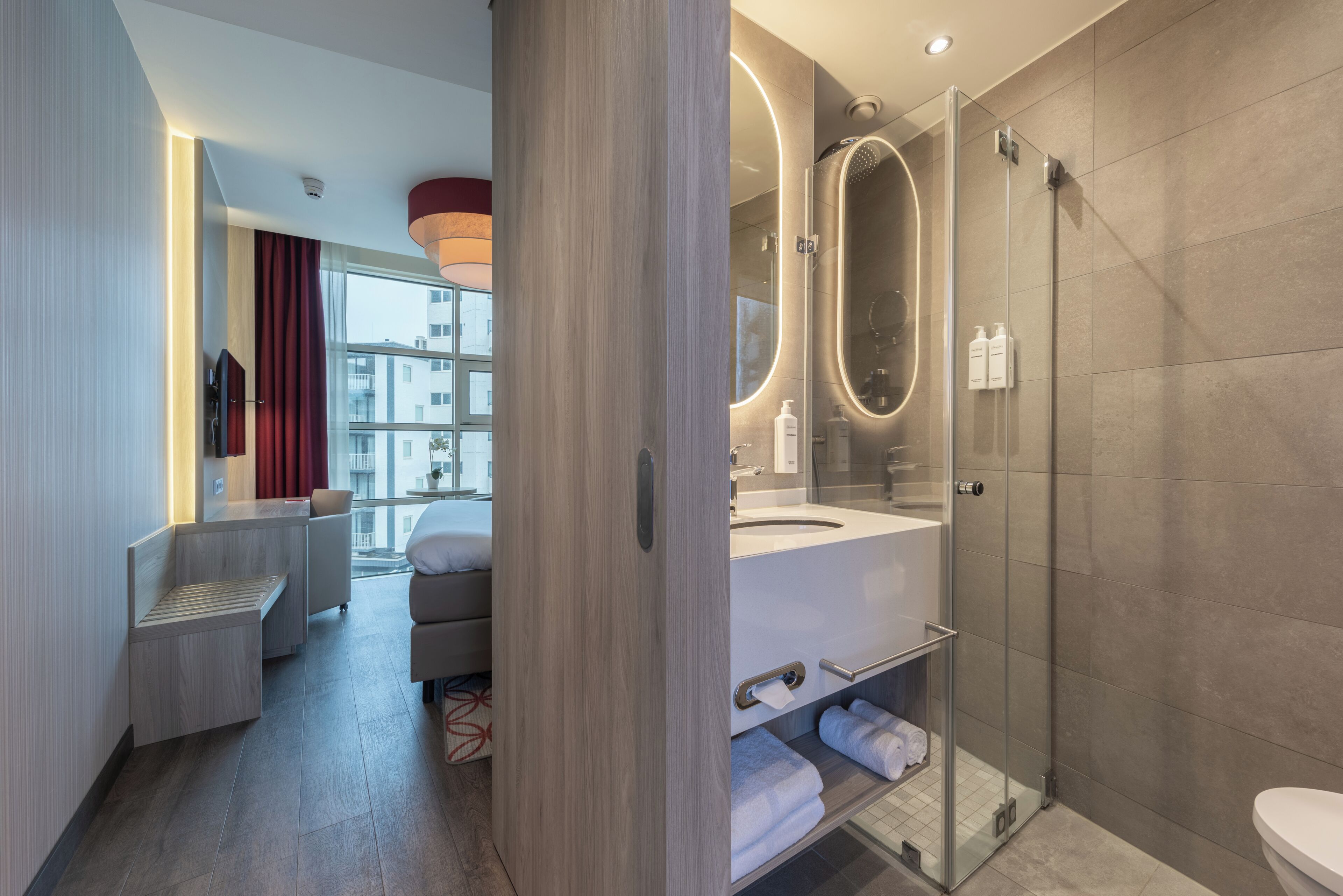 A modern bathroom with a glass shower enclosure, a vanity with a mirror, and a seating area with a bench and a chair.