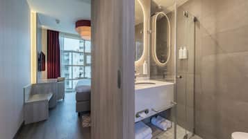 A modern bathroom with a glass shower enclosure, a vanity with a mirror, and a seating area with a bench and a chair.