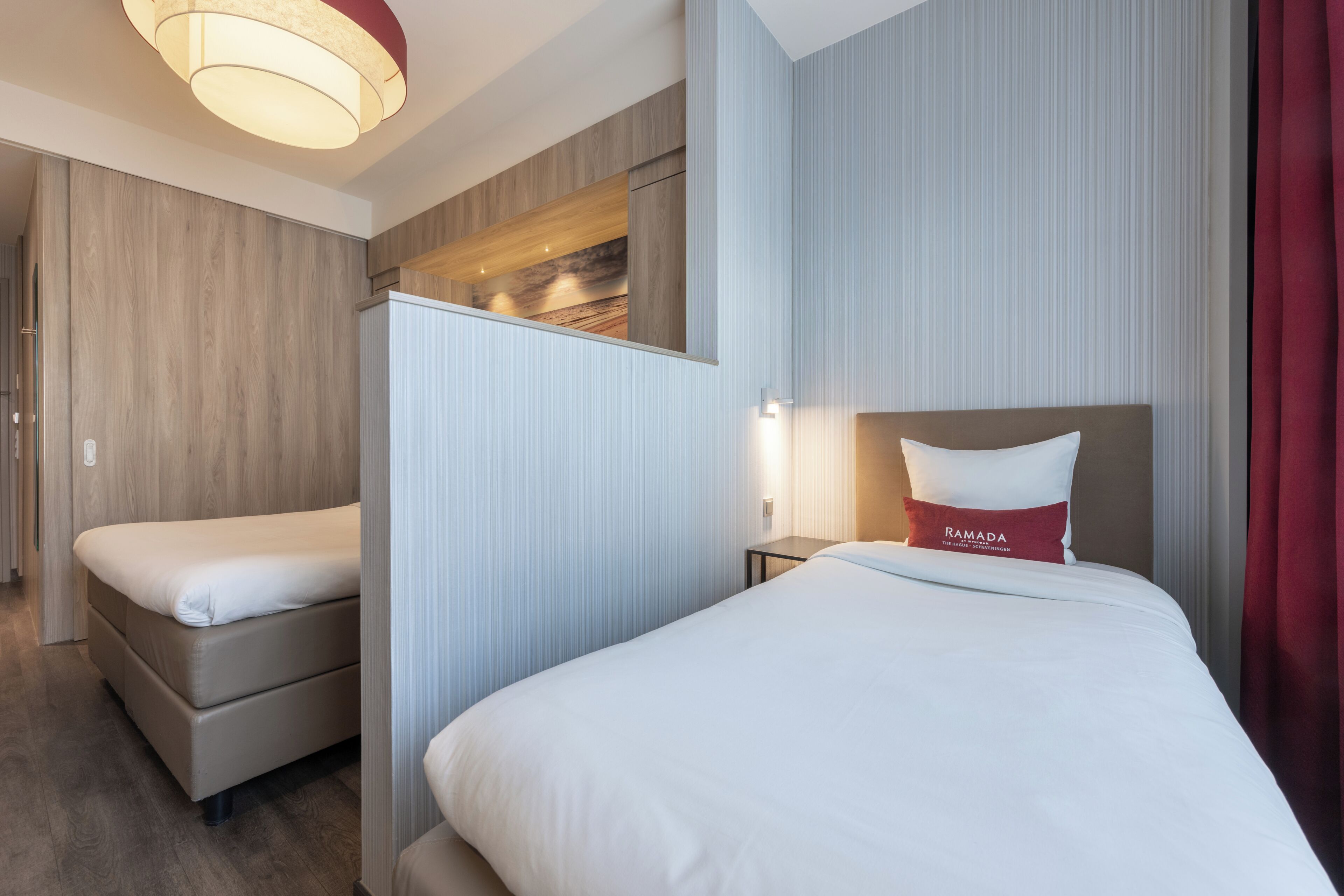 Ein Hotelzimmer mit zwei Betten, einer Wand in Holzoptik, einem roten Kissen und einer modernen Leuchte.