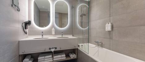 A modern bathroom with a large mirror, two sinks, a glass-enclosed shower, and a bathtub.