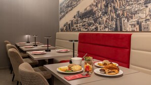 L’intérieur d’un restaurant, avec des banquettes, des tables et une fresque murale représentant un paysage urbain.