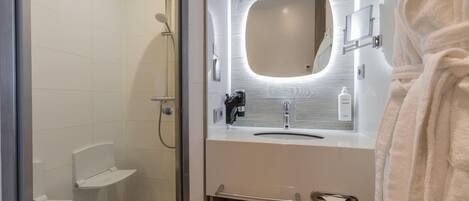 Un baño moderno con ducha cubierta por vidrio, tocador con espejo y perchero para toallas.