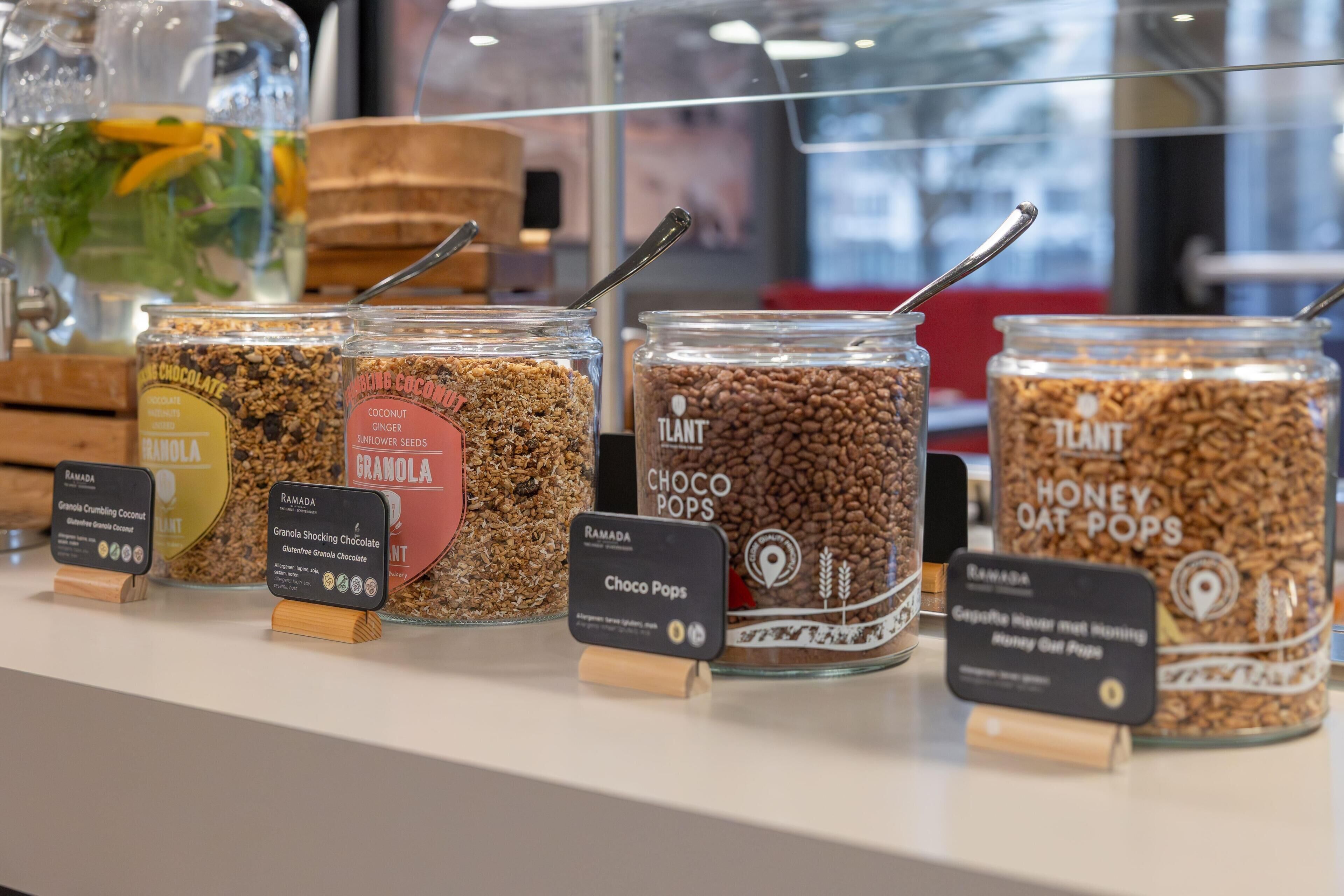 Een presentatie van verschillende granola soorten in potten, met etiketten die smaken aangeven zoals chocolade, kokos en honing haver.