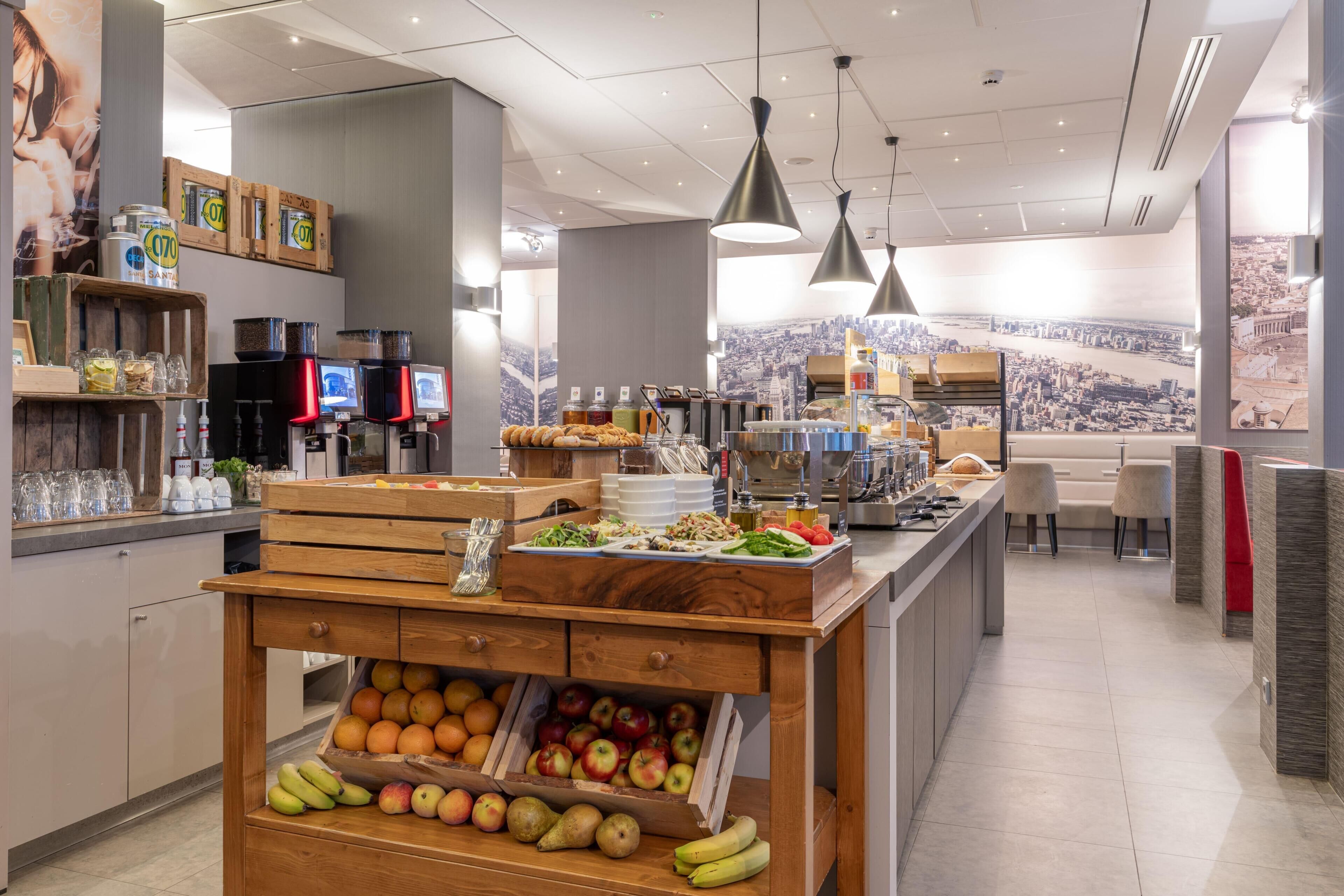 Una cafetería moderna con un mostrador central de madera que exhibe frutas y pasteles, vistas a la ciudad y un diseño limpio y contemporáneo.