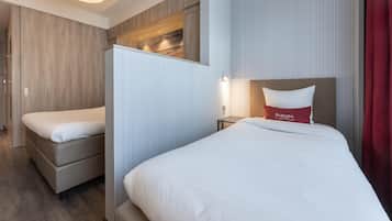 Habitación de hotel con dos camas, una mesita de noche, una lámpara de pared y vistas a la playa a través de una ventana.