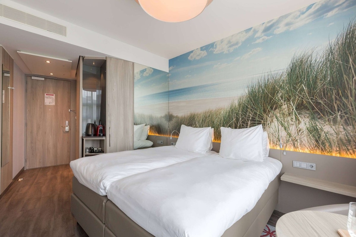 A hotel room with a bed, a desk, and a wall mural of a beach scene.