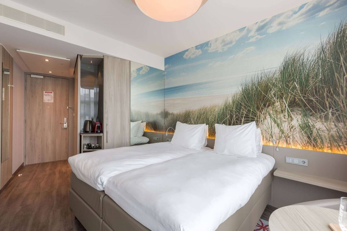 Une chambre d’hôtel avec un lit, un bureau, une armoire et une fresque murale représentant une plage.