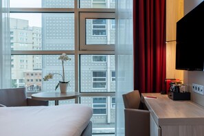 Een hotelkamer met een bed, een tafeltje met een bloeiende orchidee, een stoel, een bureau met een koffiezetapparaat en een aan de muur bevestigde televisie.