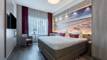 Ein Hotelzimmer mit einem Bett, einem Schreibtisch, einem Stuhl, einem Fernseher und einer großen Strandmalerei an der Wand.
