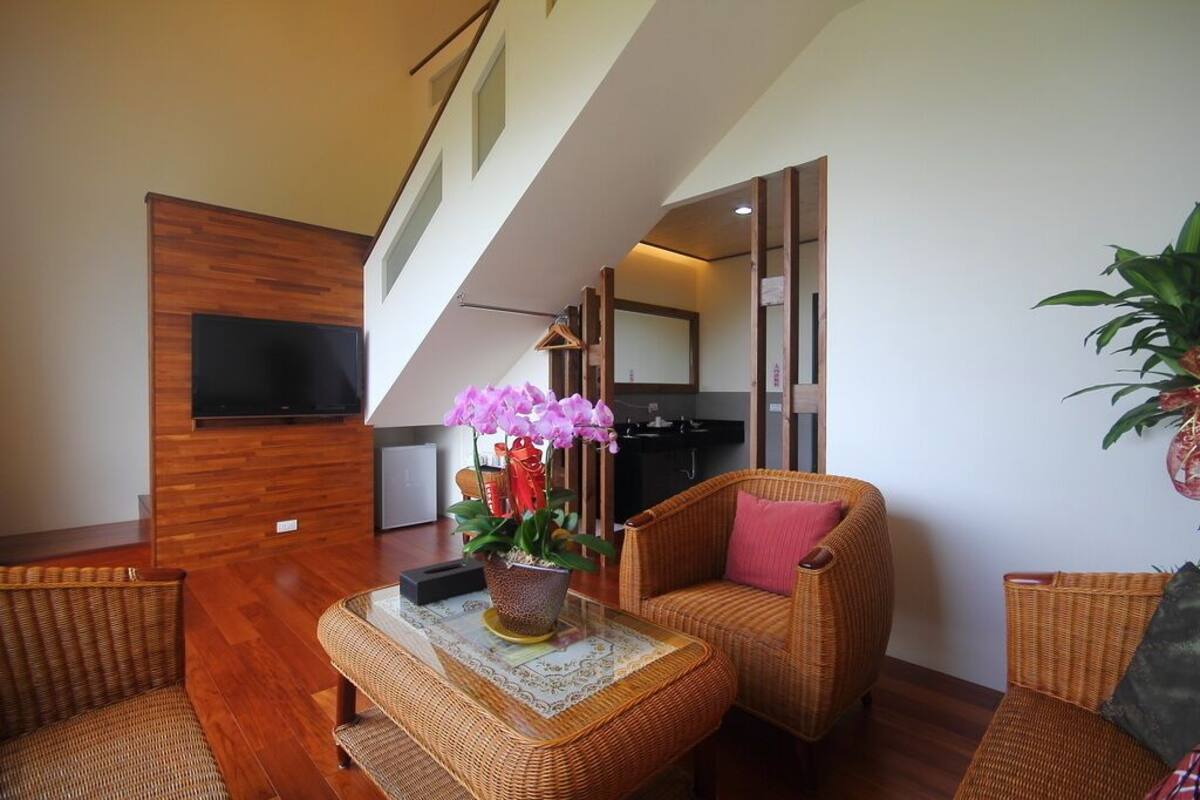 A modern living room with wicker furniture, a flat-screen TV mounted on a wooden wall, and a staircase leading to an upper level.