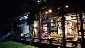 A cozy outdoor seating area with a wooden pergola, a slide, and a well-lit interior visible through large windows. - Jimei Homestay (Ji'an)
