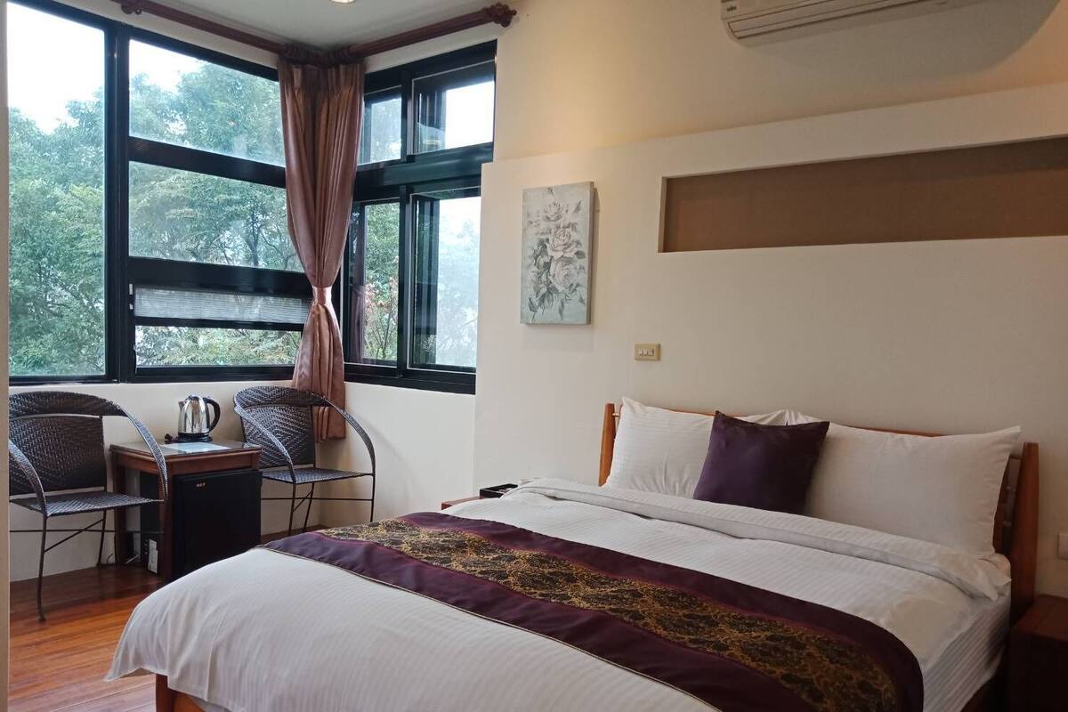 A bedroom with a bed, a chair, a small table, and a window with curtains.