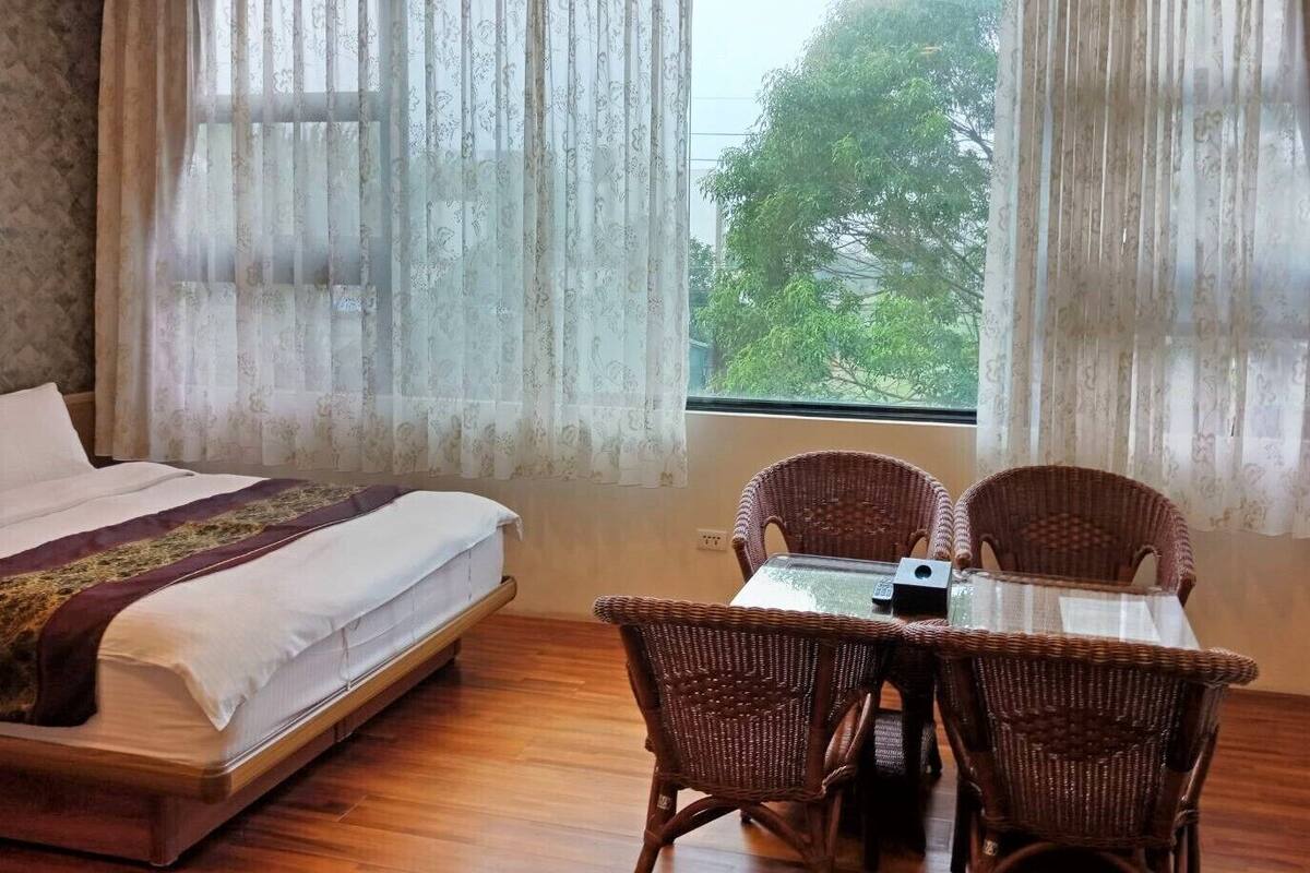 A bedroom with a bed, a table with chairs, and a window with curtains.