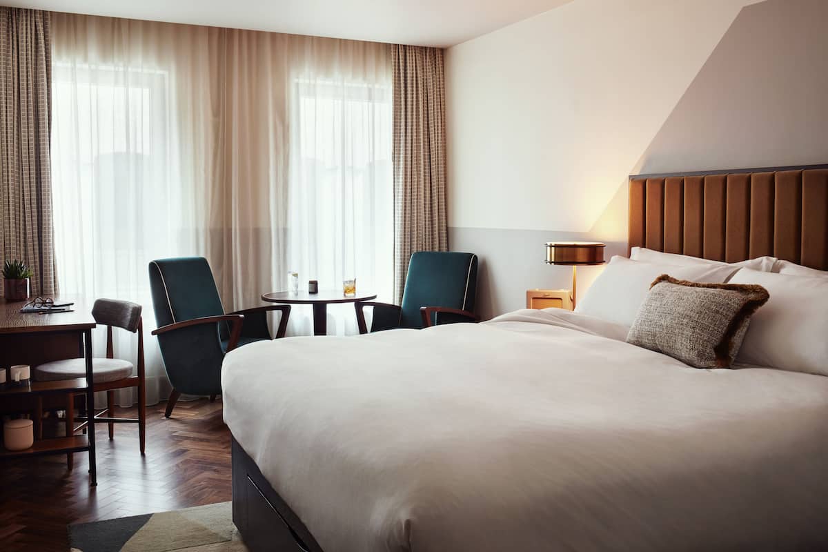 Une chambre d’hôtel avec un grand lit, deux chaises, une petite table et une lampe.