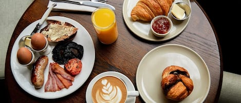 Frühstücksecke mit Croissants, Eiern, Speck, Tomaten und Kaffee auf einer Holztischplatte.