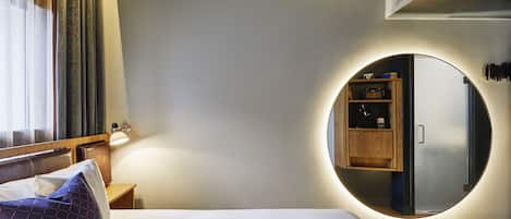 A modern hotel room with a bed, a round mirror, a nightstand, and a built-in wardrobe.