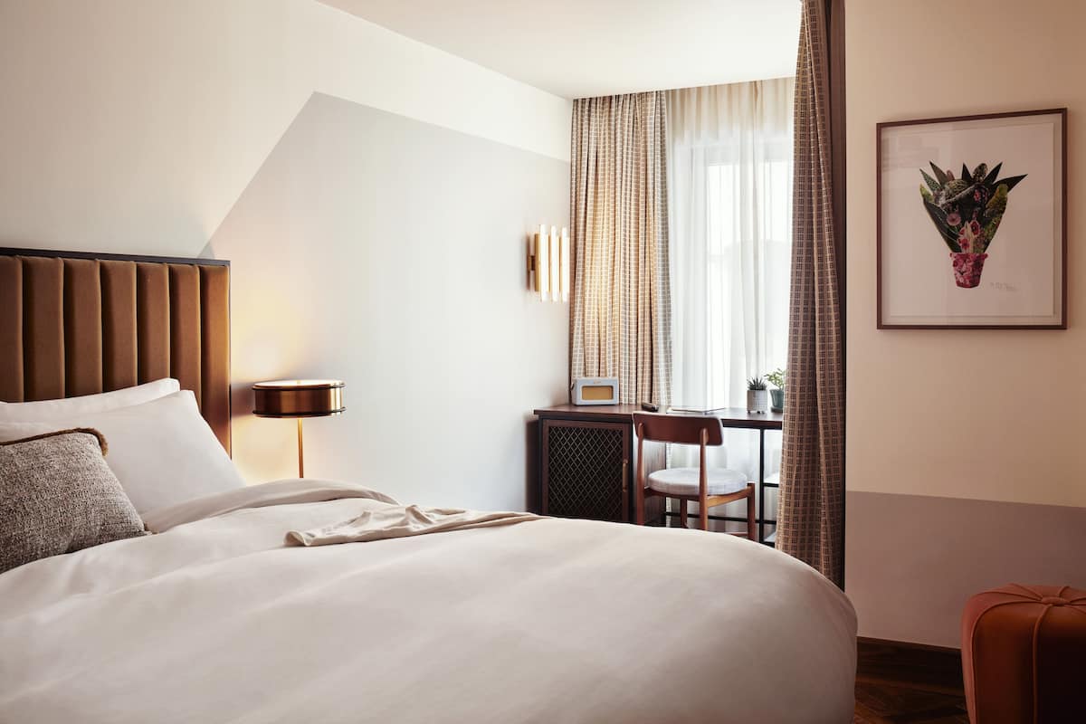 Une chambre d’hôtel comprenant un lit, une table de chevet, une lampe, une chaise, un bureau et un tableau encadré au mur.