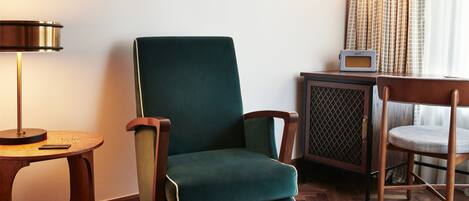 A room with a green upholstered chair, a wooden side table with a lamp, and a small radio on a cabinet.