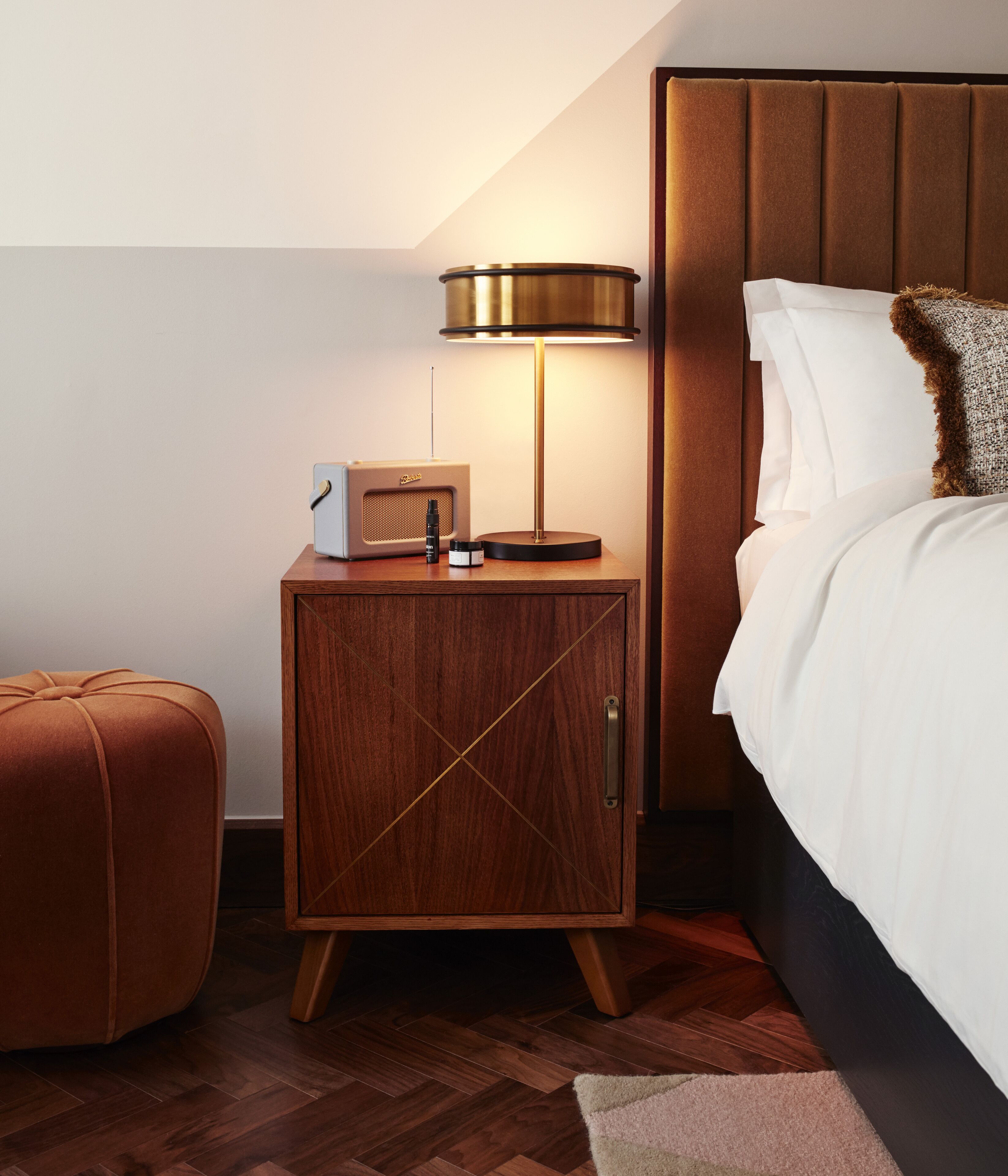 Ein ordentlich eingerichtetes Schlafzimmer mit einem Bett, einem Nachttisch mit Lampe, einem Radio und einem kleinen Schrank.