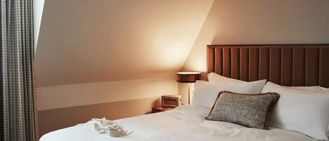 A hotel room with a large bed, a bedside table with a lamp, and a window with curtains.