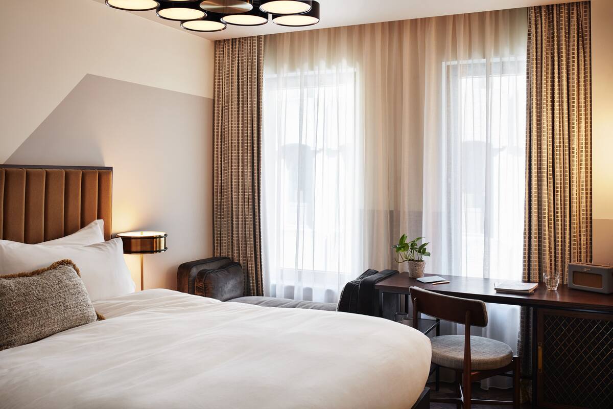 Une chambre d’hôtel avec un grand lit, un bureau avec une chaise, une petite table, une lampe et un téléviseur.