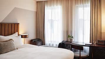 A hotel room with a large bed, a desk with a chair, a small table, a lamp, and a television.