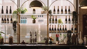 A bar with shelves of wine bottles, plants, and a window view. - The Hoxton, Holborn (London)