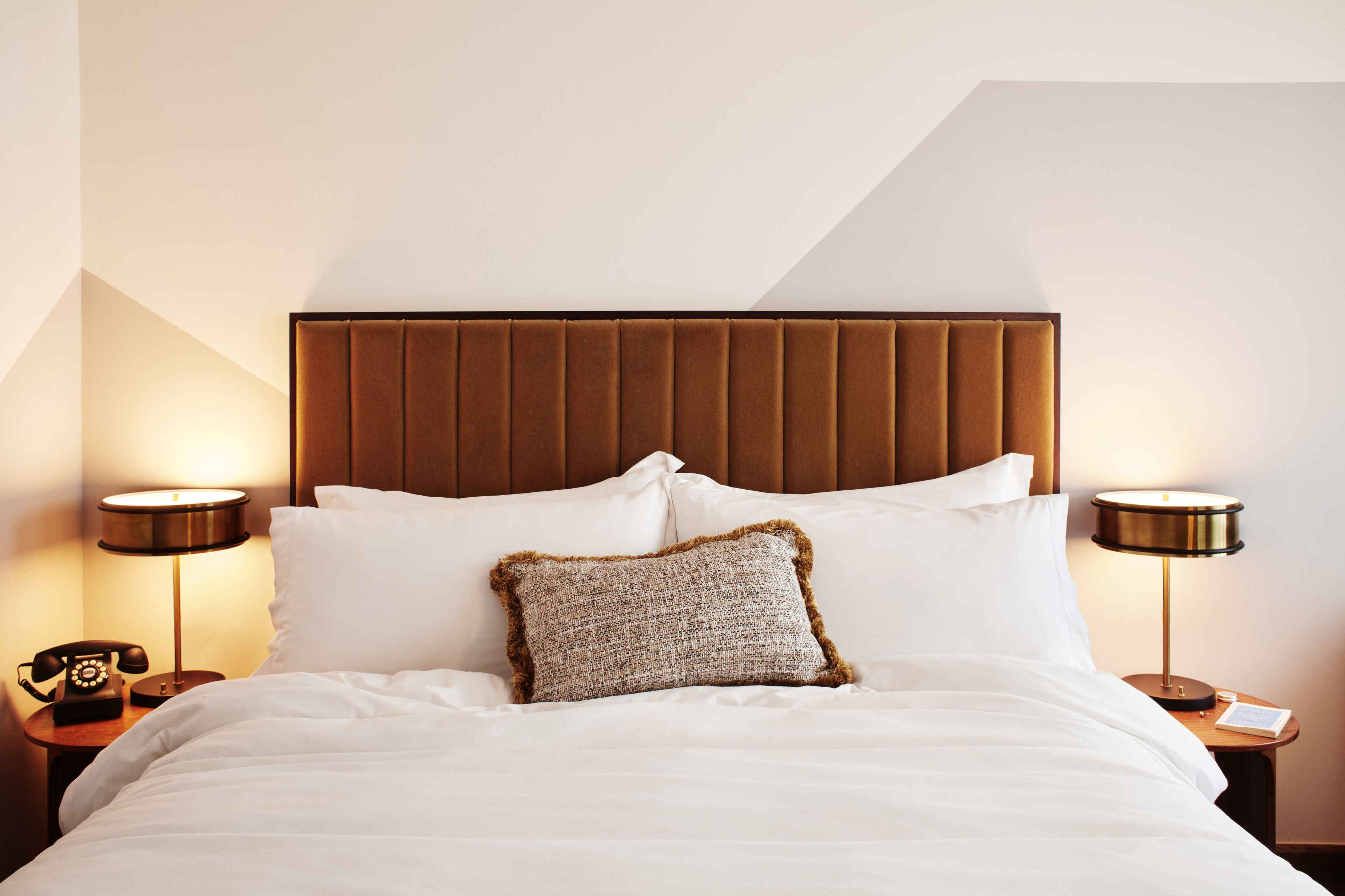 A neatly made bed with white linens, a brown headboard, and two bedside lamps on wooden nightstands.