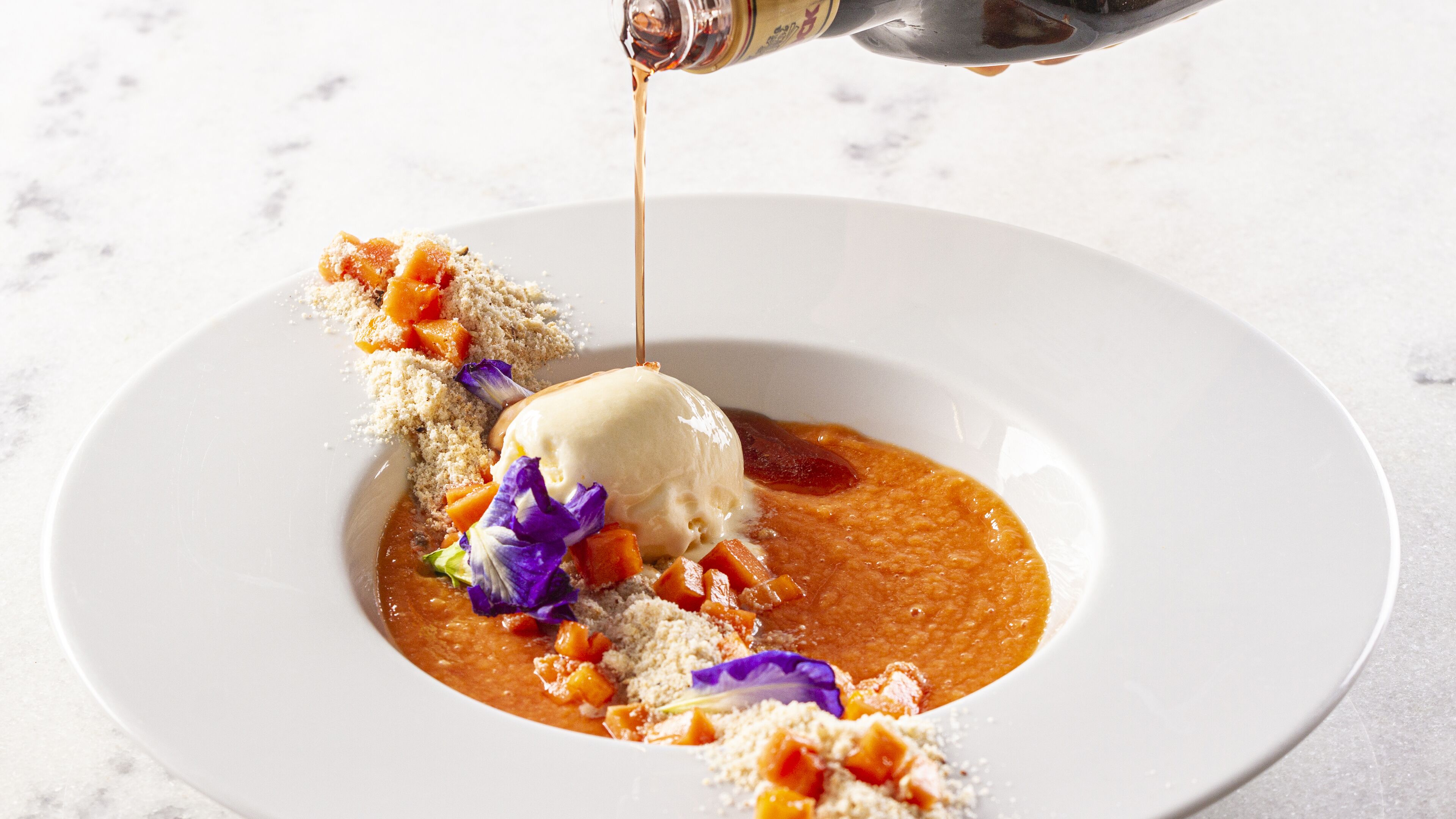 A dessert with a scoop of ice cream on a plate with a sauce and garnishes.