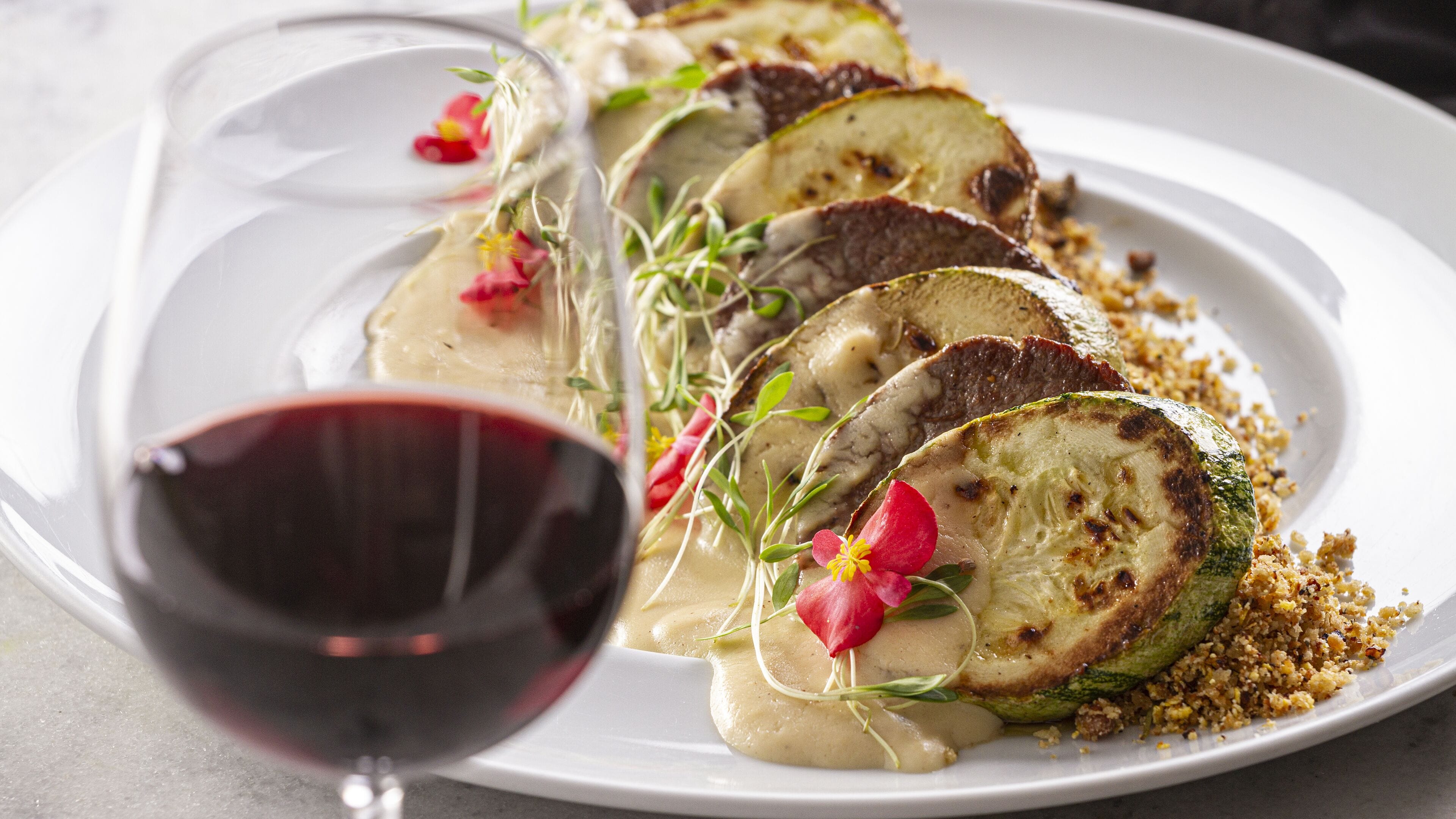 A plate of food with sliced vegetables and a glass of red wine.