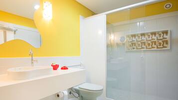 Une salle de bain avec un mur jaune, un lavabo blanc et une cabine de douche en verre.