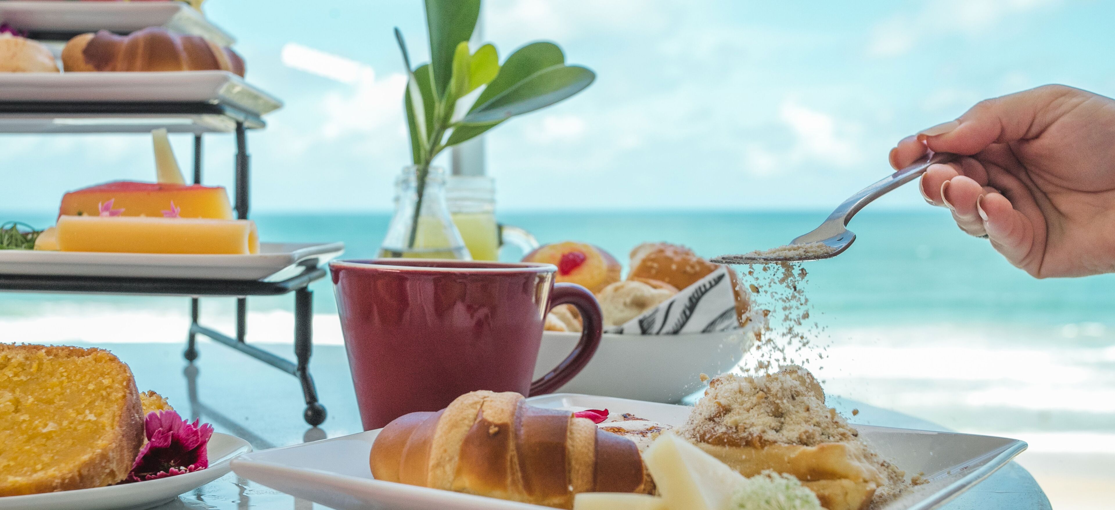 A breakfast setting with pastries and a beverage, overlooking a beach.