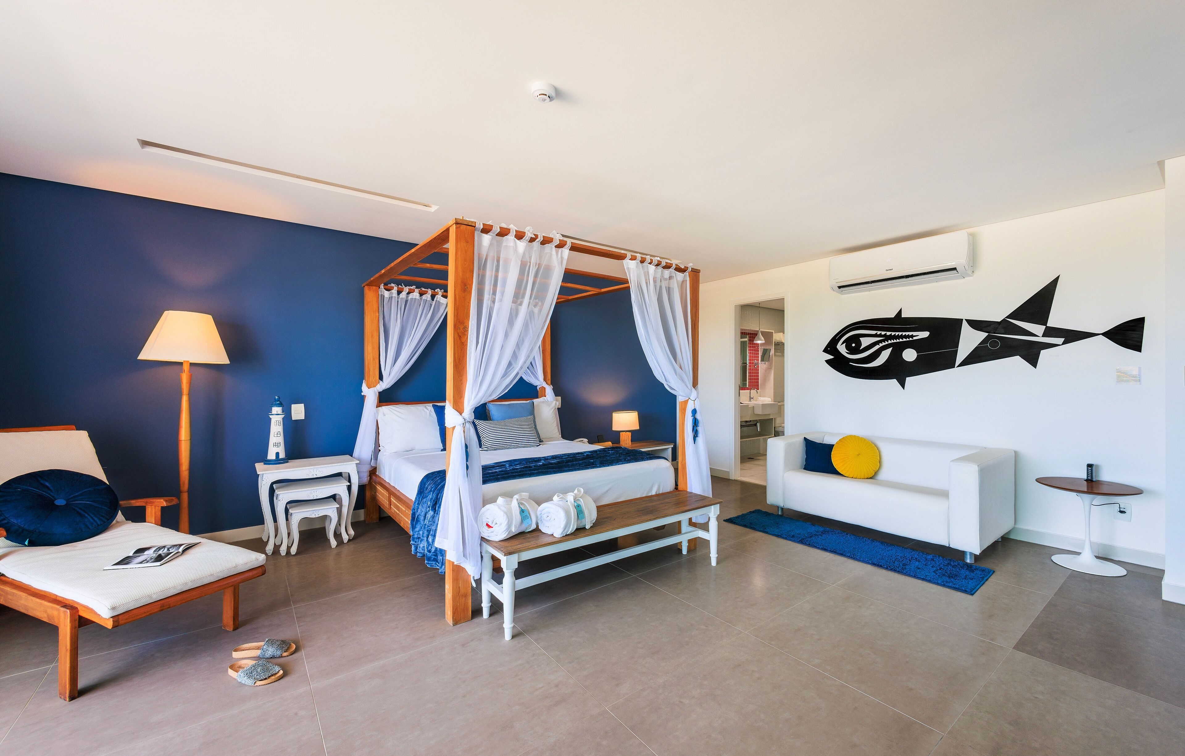 A modern bedroom with a four-poster bed, a nightstand, a bedside table, a lamp, a bench, a sofa, a small table, and a wall-mounted fish decoration.