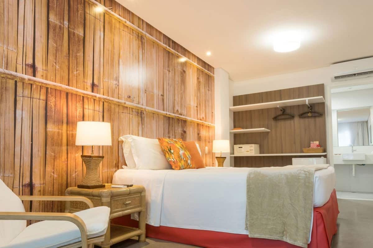 Ein Hotelzimmer mit Bett, Sessel, Nachttisch, Lampe, Kleiderschrank und Bad.