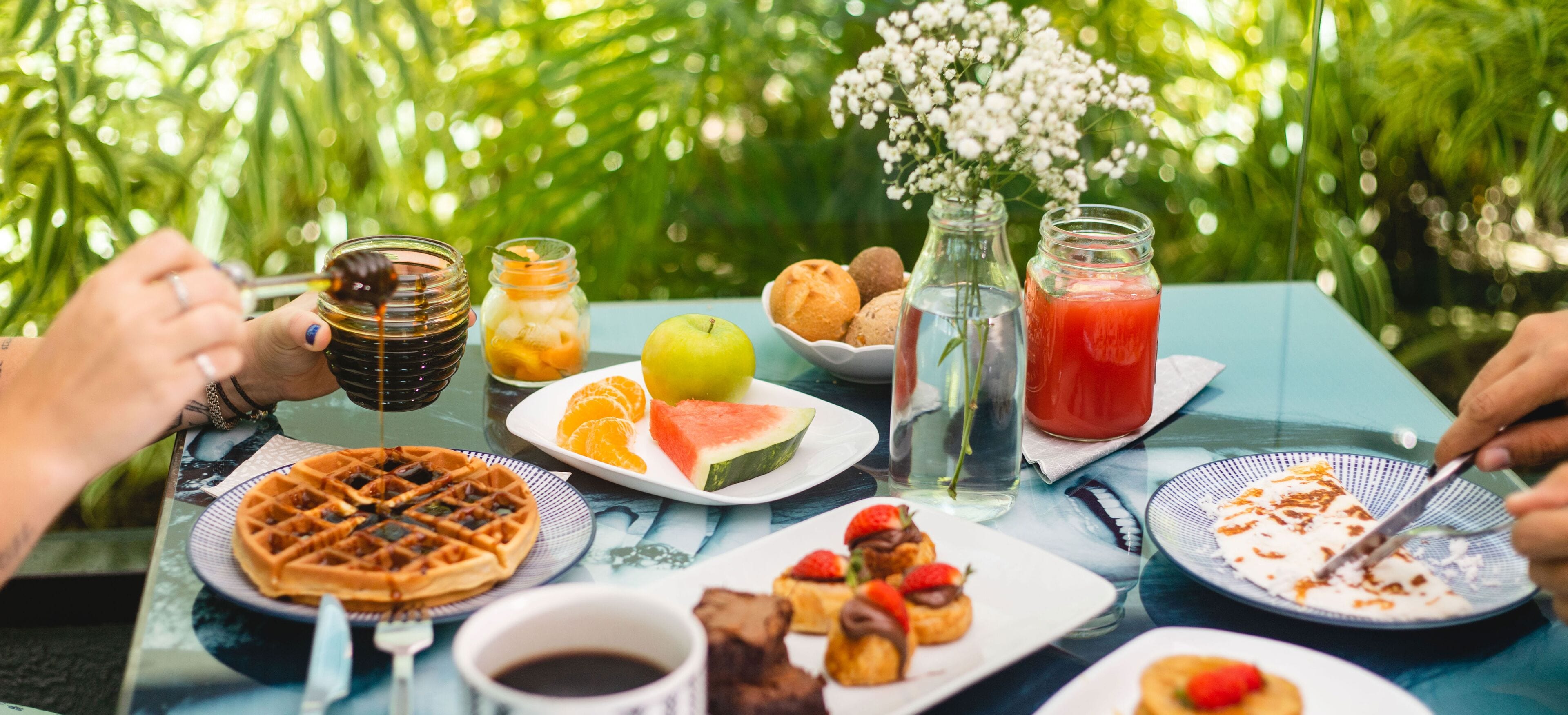 A table set outdoors with various breakfast items including waffles, fruit, and beverages.